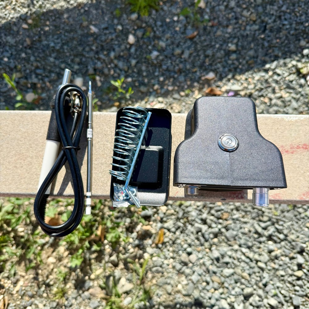 T12 soldering station parts laid out: soldering iron with cable, spare tip, iron stand and station unit